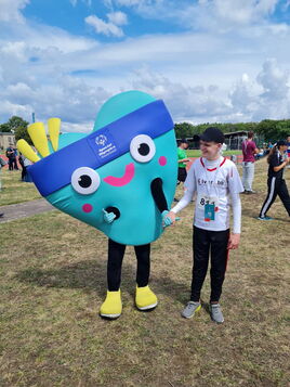 Glückliches Special Olympics Maskottchen hält Händchen mit einem jungen Athleten im Freien.