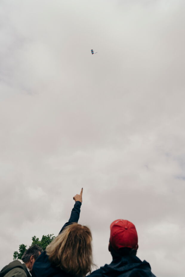 Zwei Personen schauen bei bewölktem Himmel einem Fallschirm zu, der am Himmel fliegt. Eine Person zeigt mit dem Finger darauf.