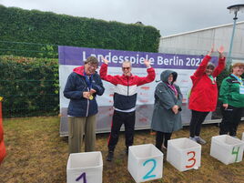 Silbermedaillen-Gewinnerin Sandra jubelt auf dem Podium neben anderen Athlet:innen im Regen.