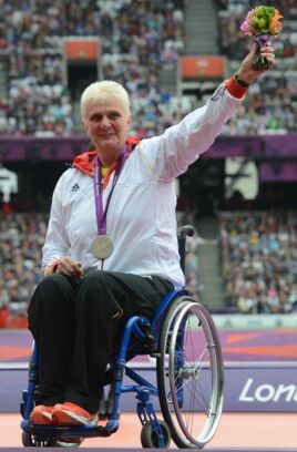 Marianne Buggenhagen im Stadion mit Goldmedaille um den Hals und stolz einen Blumenstrauß in die Luft streckend