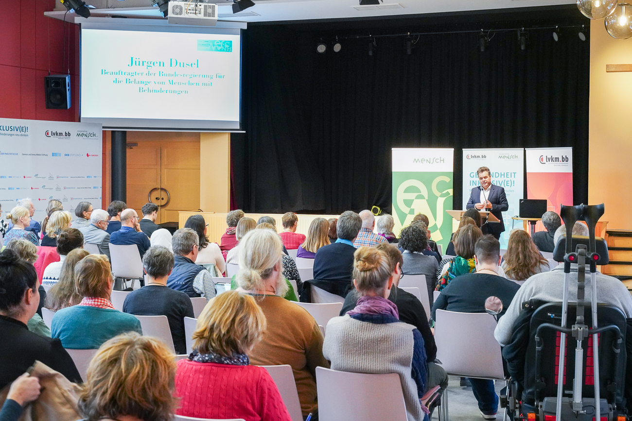 Eine Konferenz mit einem Redner und Publikum, das auf eine Präsentation schaut.